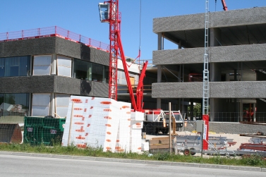 En röd byggkran mellan och framför två ännu inte fördigbyggda huskroppar, bestående av betongelement. Foto: Karin Sterner