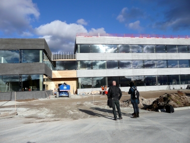 Två personer står och tittar på RAÄ:s nya lokaler i Visby, molnen speglar sig i fasaden