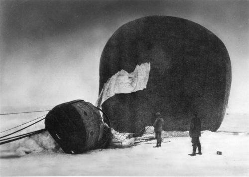 Två människor framför en luftballong som ligger på sidan i snö.