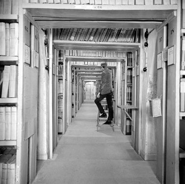 Gamla Riksarkivet, ett mer traditionellt arkiv. Arkivhandlingar med en arkivarie på en pall i bakgrunden.
