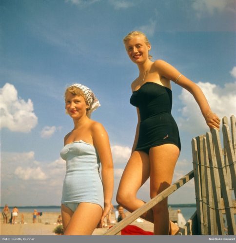 Två unga kvinnor i baddräkt på strand