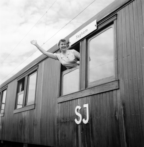 Kvinna vinkar från ett fönster i en tågvagn.